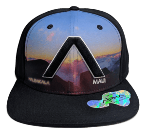 Introducing "The Haleakala - Keiki Cap": a black snapback cap designed for kids, showcasing a vibrant mountain landscape. The design features "Haleakalā" and "Maui" written near the brim and incorporates a prominent letter "A" in the center, symbolizing Aloha. A reflective sticker is affixed to the brim for added style.