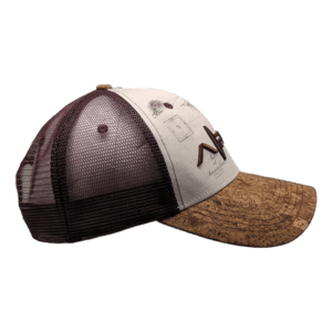 Side view of the Alpha Maui Wailea Islander trucker hat, featuring a brown and tan color scheme with a mesh back. The front showcases embroidered letters and small graphic elements on a light-colored fabric, while the brim sports a mottled pattern. Ideal for your beach apparel collection, this hat embodies an effortless Ohana vibe.