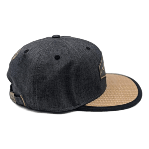 Introducing "The La Perouse" - a dark gray snapback hat featuring a light beige woven flat brim, perfect for your beach apparel collection. This hat showcases subtle embroidered details and vent holes on top. The side view highlights the contrasting textures and colors, infusing your look with a touch of Hawaii-inspired style.