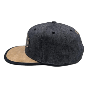 Side view of The La Perouse, a dark gray baseball cap with a tan brim and black trim. This cap features multiple ventilation eyelets on the top and sides, and an intricately embroidered "Aloha" design graces the front, though the details are not clearly visible.