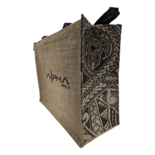 The Alpha Jute Bag is a brown, rectangular tote adorned with "Alpha Maui" branding on the side. This stylish bag showcases intricate black tribal designs along the side panel and features sturdy black handles, capturing the essence of Aloha. It’s ideal for carrying beach apparel and other essentials for your Ohana outings.