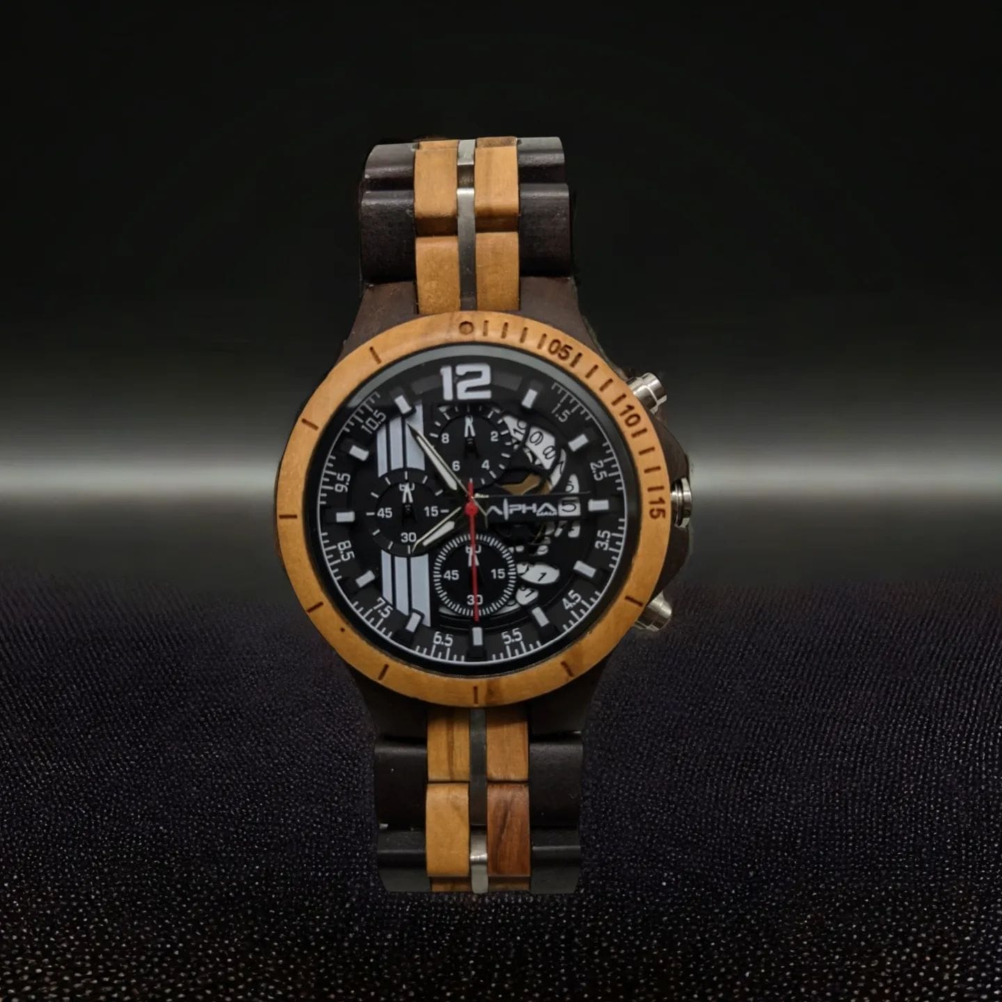 A wristwatch with a wooden band and bezel, featuring alternating dark and light wood segments. The watch face is black with silver and white numerals, markers, and hands, including three smaller dials for additional functions against a dark background. Perfect for your Alpha Maui beach apparel collection.