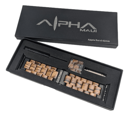 A boxed set labeled "Alpha Maui Band - Zebrawood 42mm (42-49mm)" contains a wooden watch band, a small screwdriver, and additional links for band adjustments. The packaging is black with a silver logo on the lid, and the items are neatly arranged in foam cutouts.