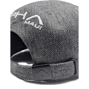 The Specialist is a gray herringbone-patterned cap, shown from the back with an adjustable strap and clip. The word "Maui" is embroidered in white, along with a logo above it. A touch of Hawaii is evident in its design, and the inside of the cap is partially visible, showcasing a soft lining.
