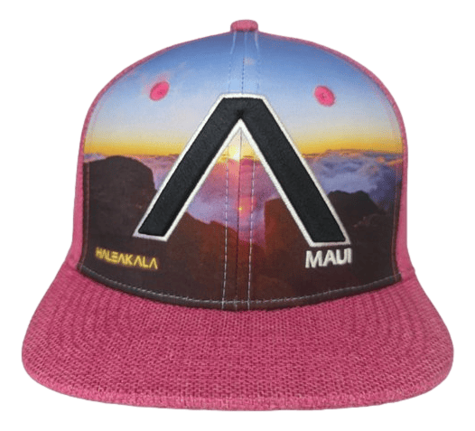 The Haleakala Pink (Kid Size) snapback cap features a vibrant sunset or sunrise scene over a mountainous landscape with bold black and white geometric shapes. The cap is adorned with the words "Alpha Maui" and "Maui" on the front, and it includes a textured pink brim and sides.