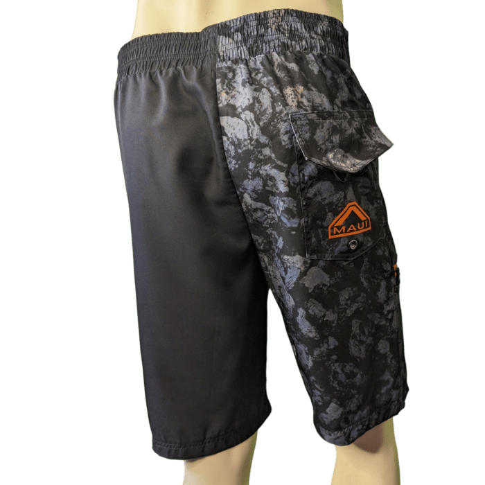 Introducing the Lava Flow men's shorts: a truly unique design where the right side is plain black and the left side features a gray camouflage pattern complete with a flap pocket. The pocket proudly displays an orange "Alpha Maui" logo. With an elastic waistband for ultimate comfort, these shorts are perfect for your next trip to Hawaii.