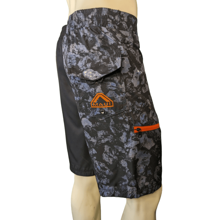 A mannequin wearing "Lava Flow" shorts, featuring a dark blue and black camouflage pattern with an orange "Alpha Maui" logo on the side pocket. The shorts have an elastic waistband and an additional small orange zipper pocket on the side. The background is plain white.