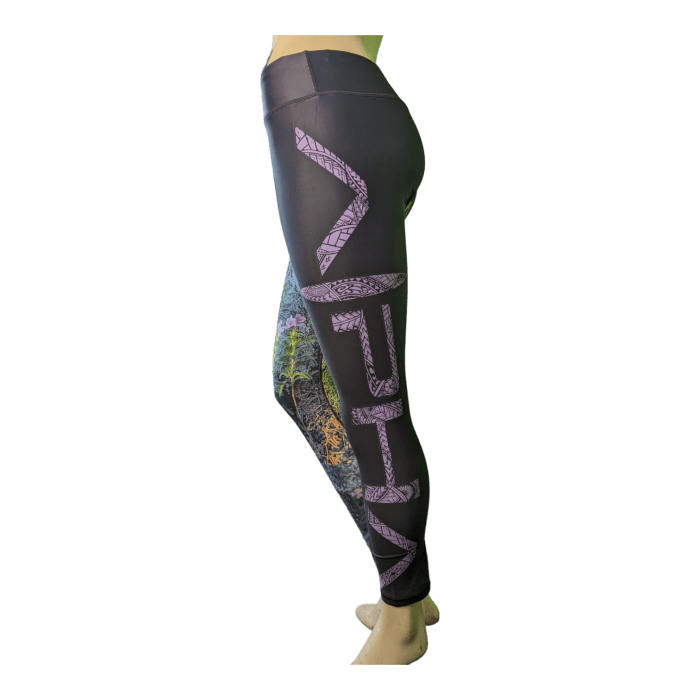 A person wearing Alpha Maui La Perouse leggings, available in 3/4 and full length, adorned with purple geometric patterns and colorful abstract designs, perfect for adding a touch of Aloha to your beach apparel. The form-fitting leggings prominently display the intricate artwork, creating a vibrant and dynamic look against a solid black background.