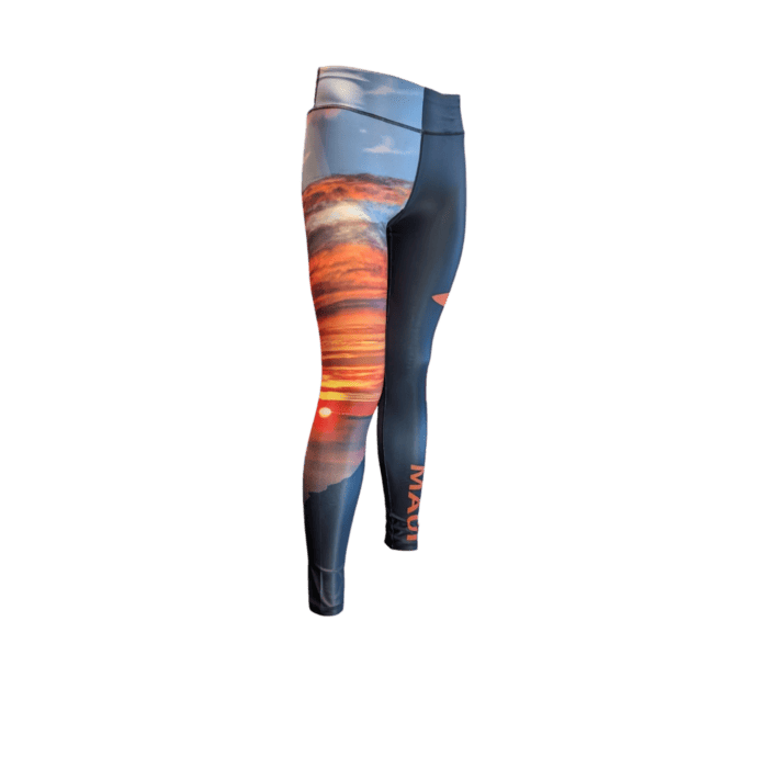 The Alpha Maui Haleakala leggings feature a vibrant sunset scene with orange and red clouds on a dusky sky. "Maui" is printed vertically in orange near the ankle for a tropical touch.