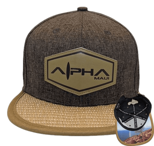 The Pali is a dark brown snapback cap adorned with a beige hexagonal logo on the front that reads "Aloha Maui." The cap features a wicker-like texture on the brim and showcases a scenic coastal landscape on the underside of the brim, making it an ideal addition to your beach apparel collection inspired by Hawaii.