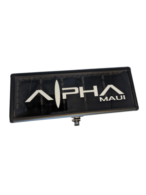 A rectangular sign with a black background displays the text "Alpha WATCH CARRIER" in white uppercase letters. The letter "L" is stylized to resemble a surfboard or fin shape, evoking a sense of Aloha. The elevated sign likely advertises watch carriers or serves as a business identifier.