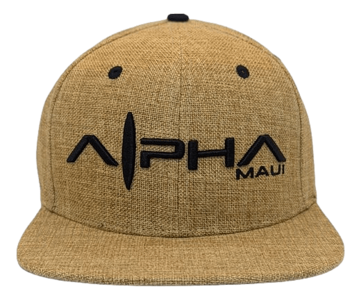 A tan baseball cap with a textured fabric design, featuring the text "Alpha Maui" embroidered in black on the front. The cap, named Hemped Out, has a curved visor, ventilation eyelets on the top, and embodies the spirit of Hawaii's Ohana.