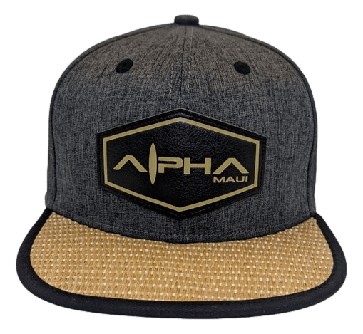 Introducing The La Perouse: a dark gray snapback hat adorned with a striking black and gold hexagonal logo reading "Alpha Maui" on the front. Ideal for your beachwear collection, it showcases a contrasting woven straw-like texture on the underside of the bill, perfectly capturing that Ohana spirit.