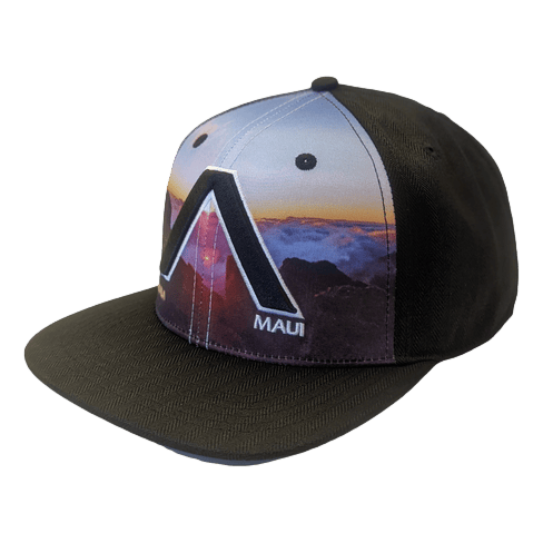 A black and multicolored cap called "The Haleakala - Keiki Cap" features a scenic sunset design on the front panel, with a large, stylized "A" and the word "Maui" printed beneath it. Branded as Alpha Maui beach apparel, the kid's cap has a flat brim and ventilation eyelets.