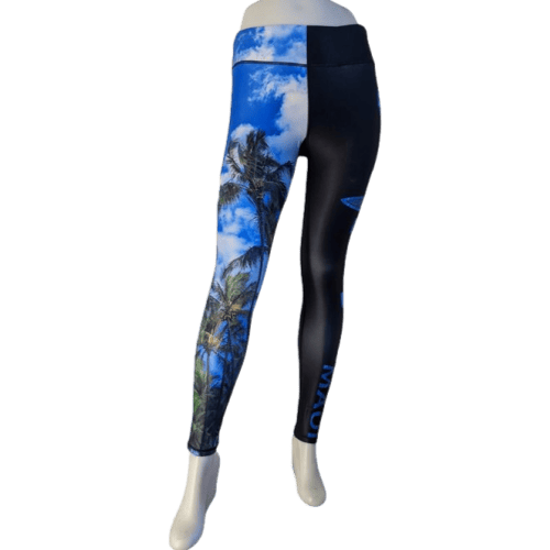 A mannequin is showcasing the Alpha Maui Hawaii (Full Length) leggings, which feature a striking design. The left leg displays a vibrant Hawaiian tropical scene with palm trees and a bright blue sky, while the right leg is predominantly black with subtle blue accents and "Alpha Maui" text details.