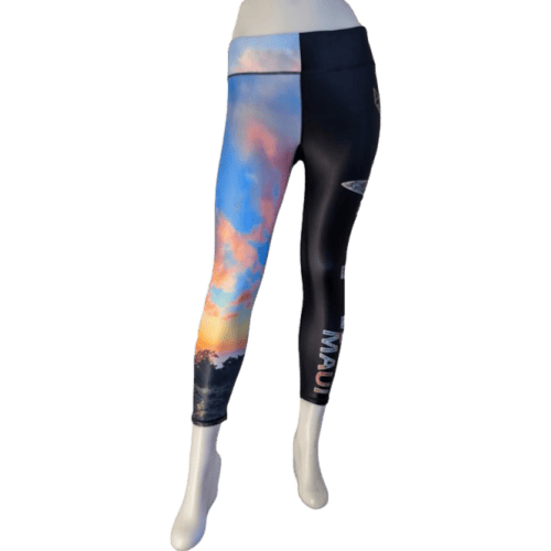 A pair of Alpha Maui Ulupalakua (3/4 Length) women's leggings featuring a colorful image of a sunset on one leg and a sleek black design with a surfboard logo and the word "Maui" on the other. Perfect for beach apparel, these leggings are displayed on a mannequin, capturing the vibrant spirit of Hawaii and the Aloha lifestyle.