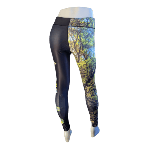 The mannequin showcases the Alpha Maui Pepe'opae (Full Length) leggings, designed with a nature-inspired motif that's perfect for beachwear in Hawaii. The left leg is primarily black, contrasting with the right leg, which features a lively forest scene of green trees and sunlight streaming through branches. The leggings have a snug fit that accentuates the shape of the mannequin's legs.