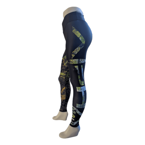 A pair of mannequin legs is adorned with the Alpha Maui Pepe'opae Full Length leggings in black and camouflage print. These leggings feature bold geometric patterns and the text "VATA" running vertically down the leg. Positioned sideways, the mannequin highlights the stylish design, delivering a trendy Aloha vibe that's perfect for your next Hawaii adventure.