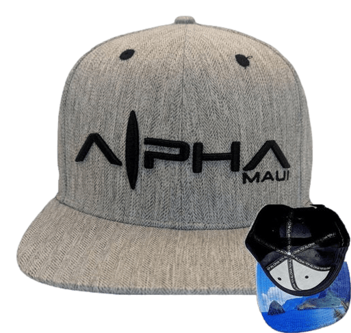 The Tinsman is a gray snapback hat featuring black embroidery that spells "Alpha Maui" on the front. Two black ventilation holes are visible at the top. The interior of the hat, shown in a small overlay, displays a blue ocean print, making it a perfect addition to your beach apparel collection and reminiscent of Hawaii's Ohana spirit.