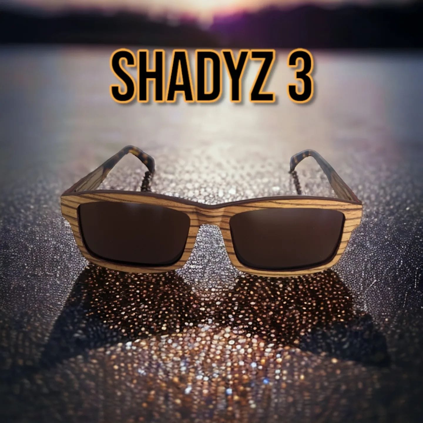 A pair of wooden-framed sunglasses, perfect for beach apparel, is displayed on a reflective surface with a blurry sunset in the background. The text "SHADYZ 3" stands out prominently above the sunglasses in bold letters, capturing the Aloha spirit.