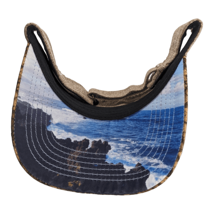 A close-up of the underside of an Alpha Maui Mauka baseball cap's brim, showcasing a printed image of a rocky coastline with waves crashing against the rocks. The visible stitching curves along the edge, and the black background highlights the details of this beach apparel piece.