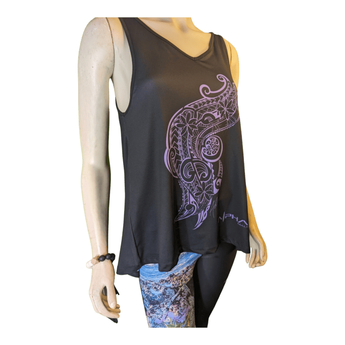 The mannequin showcases the Alpha Maui U'i Tank, a sleeveless black top adorned with an intricate purple design on the left side, embodying a relaxed Aloha vibe. It is stylishly paired with multicolored patterned leggings, and the mannequin's left arm is accessorized with a black beaded bracelet.