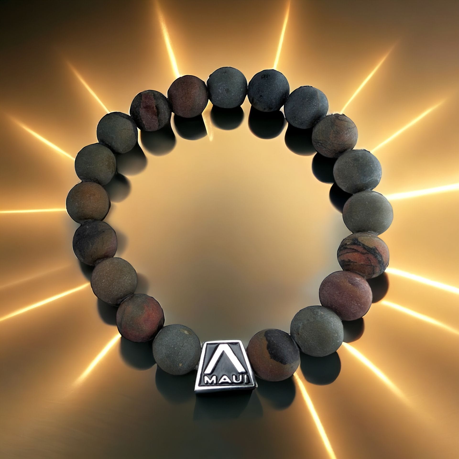 A beaded bracelet with round, multicolored stones and a metal charm engraved with the word "Alpha Maui" is arranged in a circle on a gold background with radiating light effects.