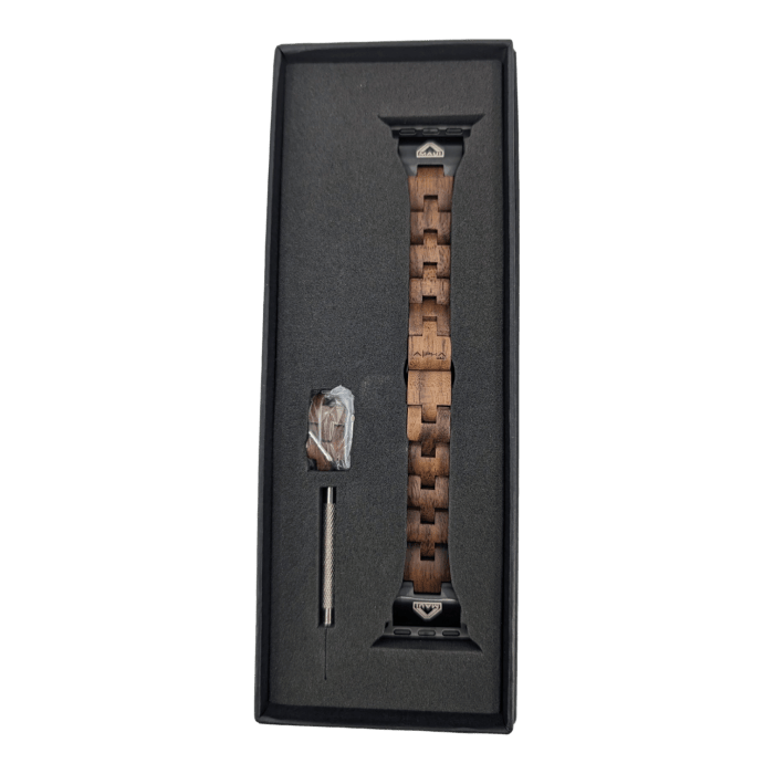 The Alpha Maui The Haleakalā, a brown wooden Apple Watch strap with metal connectors, is showcased inside a black box. Included in the package are a small screwdriver tool and additional hardware, likely for adjusting the strap length. Designed with an Ohana touch, the box features a foam insert to securely hold all contents.