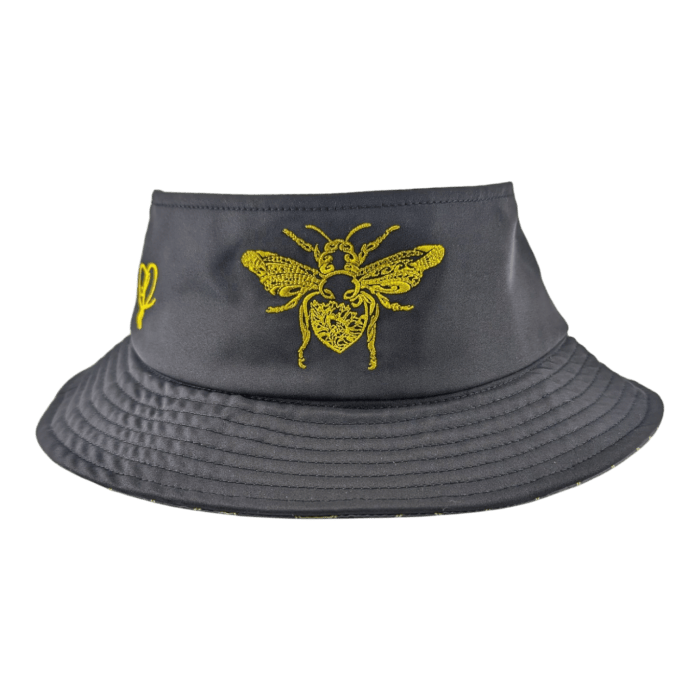 Introducing the Alpha Maui Bee Bucks: a dark gray bucket hat adorned with a vibrant yellow embroidered bee design on the front. The bee, complete with intricately detailed wings, is beautifully positioned above a charming heart motif. This hat features an Ohana-inspired wide, subtly textured brim and surprises with a contrasting yellow pattern on the interior.