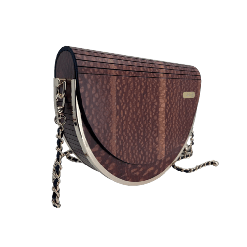 Introducing the Alpha Maui Pu'olo Handbag, a chic, half-moon-shaped accessory boasting a dark woodgrain pattern with striking vertical grooves. It comes complete with a gold chain strap and proudly displays a small gold Alpha Maui emblem on the side. The bottom edge is elegantly finished with shiny metallic trim, making it the ideal choice for an Aloha evening in Hawaii.