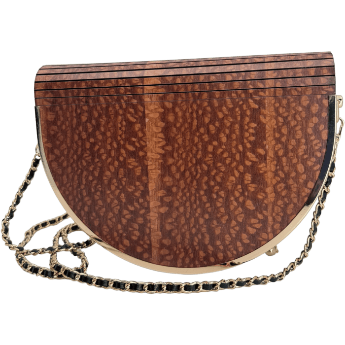 The Alpha Maui Pu'olo Handbag is a semi-circular, textured brown clutch purse with a woodgrain pattern and thin horizontal lines at the top. It features gold-toned trim and a matching gold chain strap, making it perfect for pairing with your beach apparel or transporting you to a relaxed Ohana vibe in Hawaii.