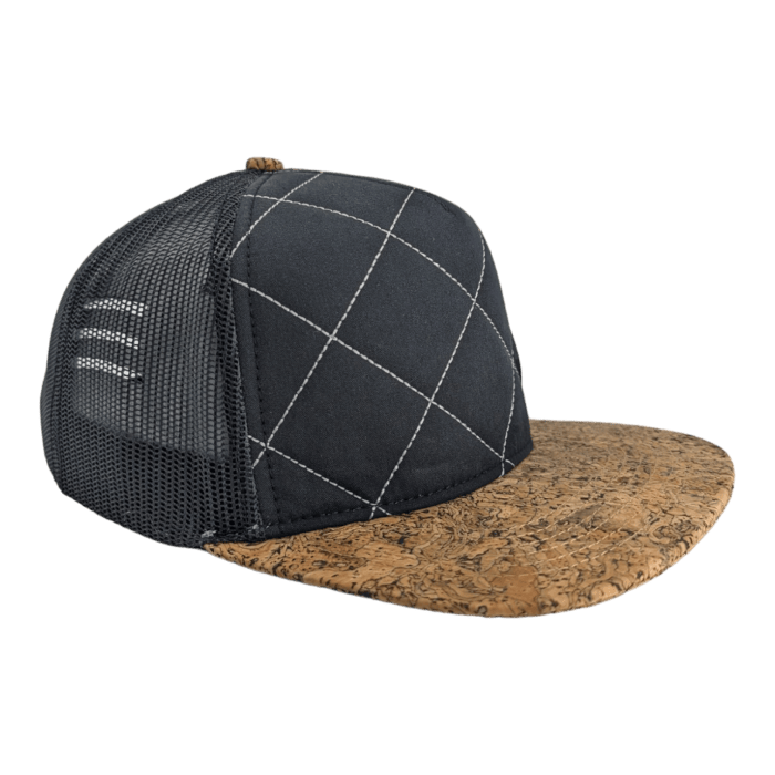 A black trucker hat with white stitching in a diamond pattern on the front panel, a black mesh back, and a brown brim with a cork texture, embodying the spirit of Ohana.