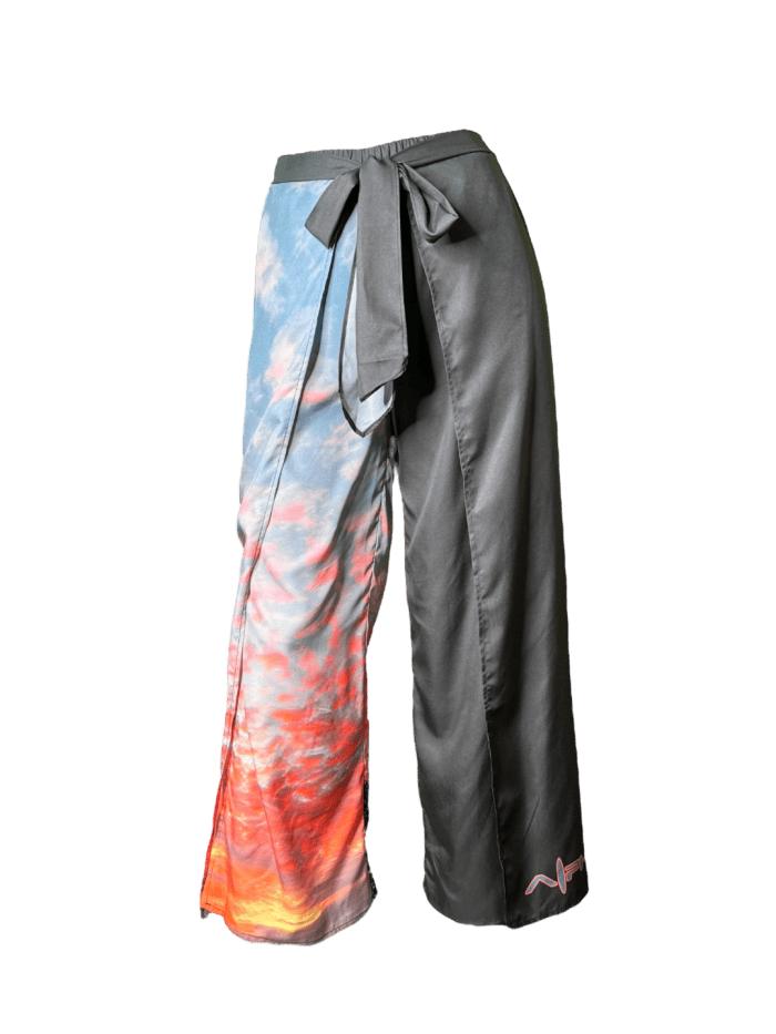 Introducing the Alpha Maui Pukalani Wrap Pants, a pair of unique wide-legged pants featuring a stunning split design perfect for beach apparel. The left leg boasts a vibrant sky and cloud print transitioning from blue to orange, capturing the essence of an Alpha Maui sunset, while the right leg is solid black. These pants are completed with a stylish tie-waist closure.