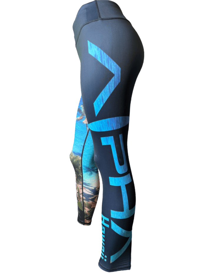 An image showcasing an individual in dark, form-fitting Alpha Maui Waimanalo leggings, adorned with blue and white "HPH" logos and text, as well as vibrant tropical beach scenes on the thigh. These full-length leggings are ideal for beachwear and perfectly capture the essence of Ohana.