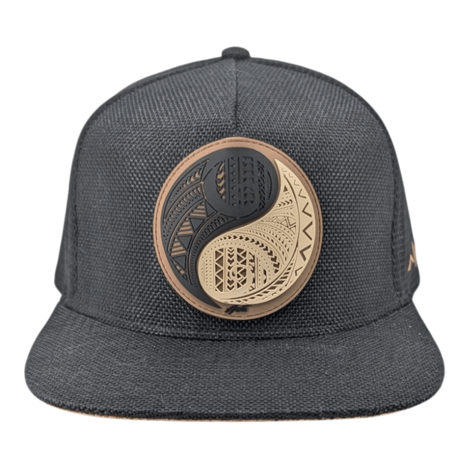 The Alpha Maui The Balance is a black flat-brim hat with a prominent gold and black round emblem featuring intricate geometric and tribal patterns on the front panel.