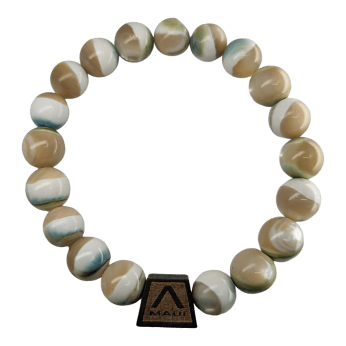 Introducing the Shell Pearlet: a beaded bracelet adorned with round, multicolored beads in shades of beige, white, and light green. The bracelet is elegantly crafted with a small, rectangular wooden charm etched with the inscription "Maui" and featuring a triangular logo. This accessory beautifully encapsulates the essence of Hawaii's Aloha spirit.