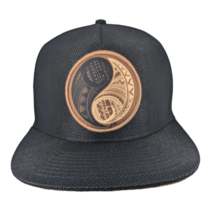 The Balance is a black baseball cap showcasing an intricate, circular design on the front. This detailed design incorporates geometric patterns in earthy tones, creating a visually appealing focal point on the hat. The cap also features a flat brim and textured fabric for added style.