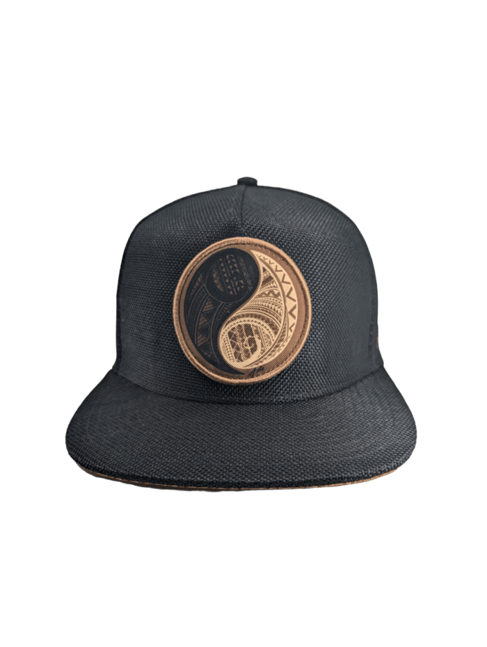 The Balance cap showcases a flat brim and solid black background, adorned with a brown and black embroidered yin-yang symbol on the front panel. The yin-yang design includes intricate patterns within each half of the circle.