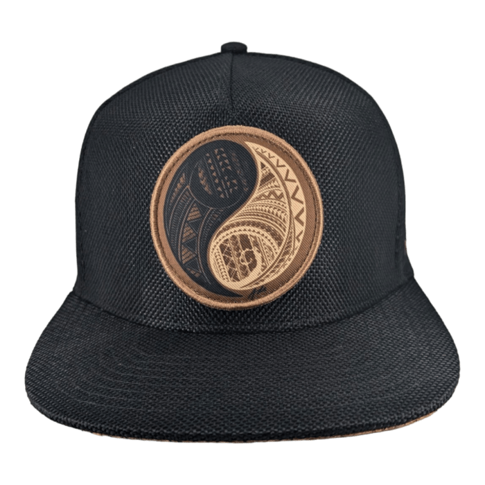 The Balance is a black snapback hat showcasing a meticulously embroidered design on the front. The design features a circular yin-yang symbol with intricate geometric patterns and textures in shades of brown and black, offering a unique and stylish appearance.