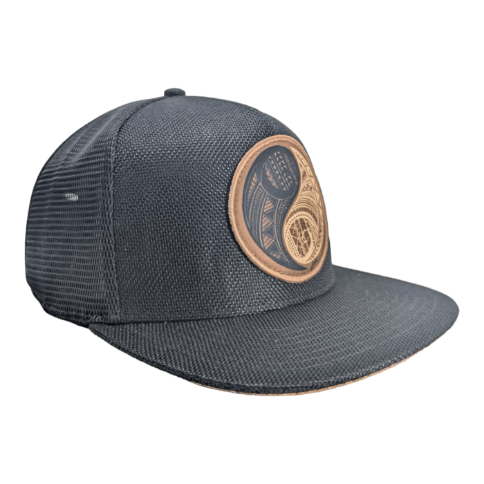 The Balance is a dark gray snapback hat with a flat brim and a mesh back. It features a circular embroidered patch on the front, showcasing an intricate design with multiple shapes and patterns in a brownish hue against a plain black background.