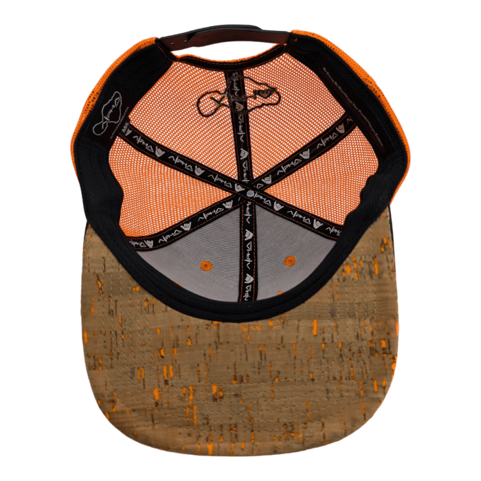 The underside of the Lava Loaded cap showcasing its interior design. The cap features a hexagonal orange and grey fabric pattern, alongside an adjustable strap. The top includes a black strip with white text running along the seams, and there's a light brown cork brim with speckles.