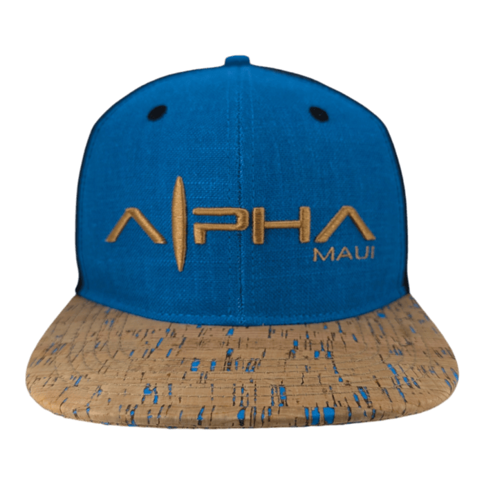 The Coastline is a blue baseball cap featuring "ALPHA MAUI" embroidered in gold on the front, with a cork-patterned brim accentuated by blue detailing and two ventilation holes on the front panel.