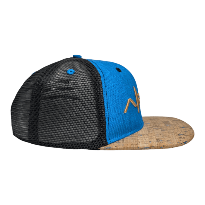 Side view of The Coastline, a stylish trucker hat featuring a blue front panel and a black mesh back. The hat has an angular design on the side and a brown cork-like visor with subtle pattern details.