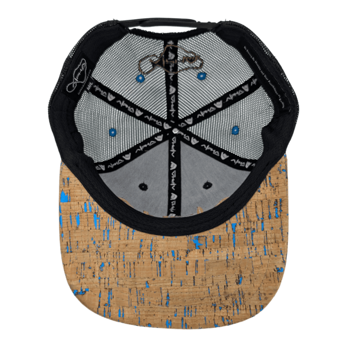 The underside of The Coastline baseball cap boasts a cork-patterned brim adorned with blue speckles, a black interior featuring white Avo logos, and fabric panels in greenish-gray with a stitched signature visible on one. Additionally, the cap includes triangular panel sections highlighted with black detailing.