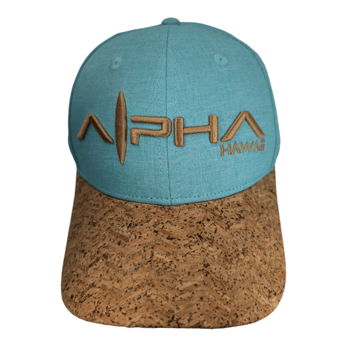 A light blue baseball cap, named Turtle Cove II, with a cork-patterned brim. The front showcases the text "ALPHA HAWAII" in a stylized, golden font.