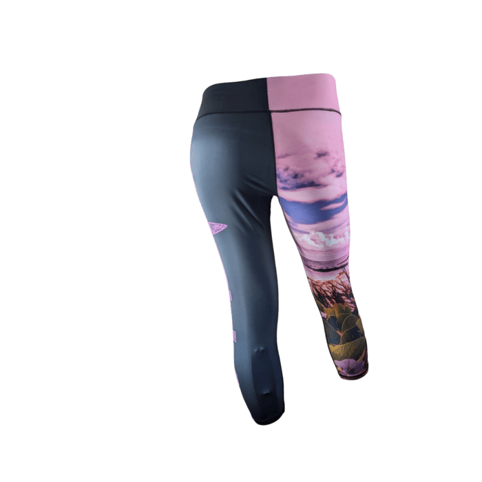 A pair of Pohuehue leggings displayed against a black background. The left half of the Pohuehue leggings is dark colored, while the right half features a vibrant nature scene with pink skies, clouds, and green foliage. The waistband is high and solid black.