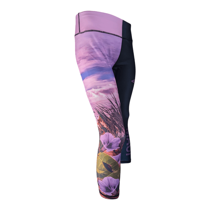 Introducing the Pohuehue leggings: a pair of fitted leggings with a vibrant design. The upper part is predominantly pink, transitioning into a nature-themed pattern adorned with flowers, leaves, and grasses in hues of purple, pink, and green. A contrasting black section on the side adds an extra touch of style to these striking leggings.