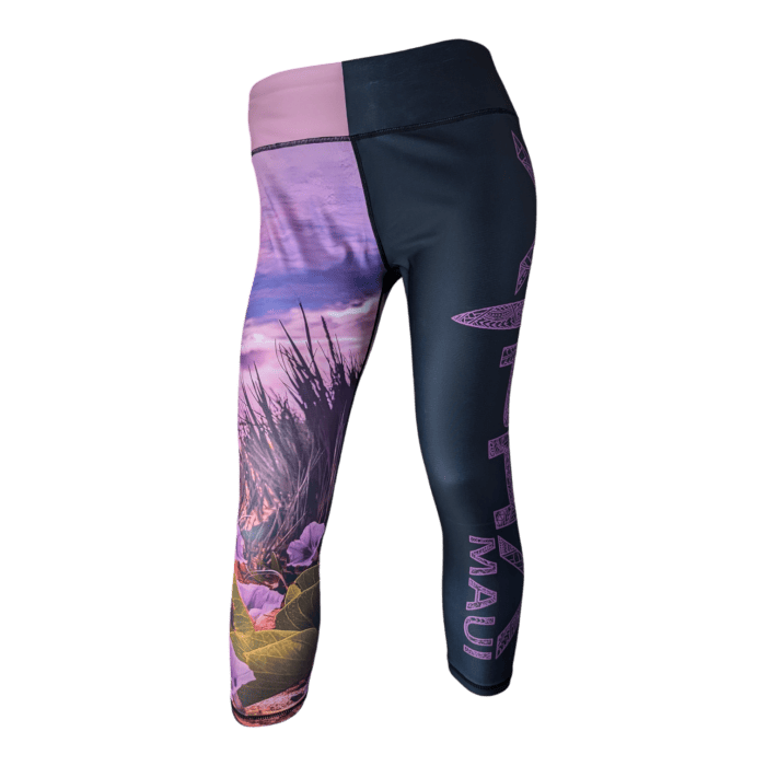 A pair of Pohuehue leggings with a vibrant design. The left leg features a colorful nature-themed print with flowers and plants near a body of water, while the right leg is predominantly dark with a vertical text reading "MAUI" and artistic patterns.