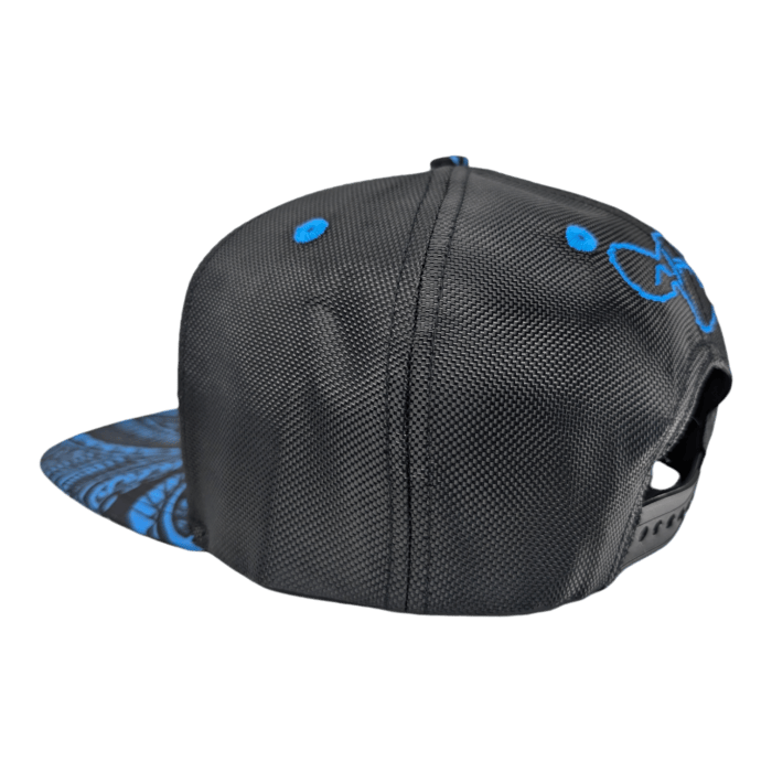 The Tribal Wai is a snapback cap featuring a black base with blue embroidered designs on the side and blue accents on the top. Its brim is adorned with a blue patterned print underside. For a perfect fit, it comes with an adjustable strap at the back, all set against a sleek black background.