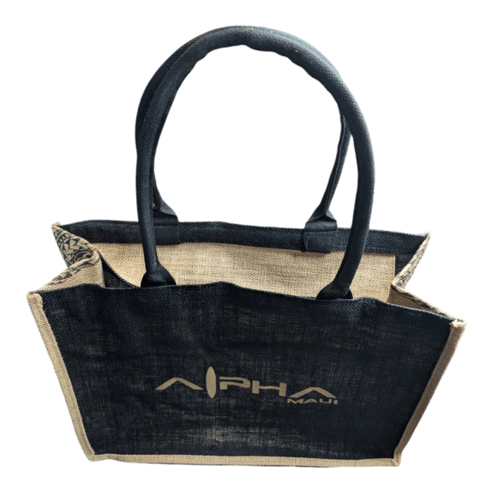 The Tribal Wai jute tote bag features black fabric handles and sides. The front and back panels are adorned with a design that includes the text "ALPHA" and "Maui" in white lettering. This bag has a rustic texture, a boxy shape, and a partially visible interior.